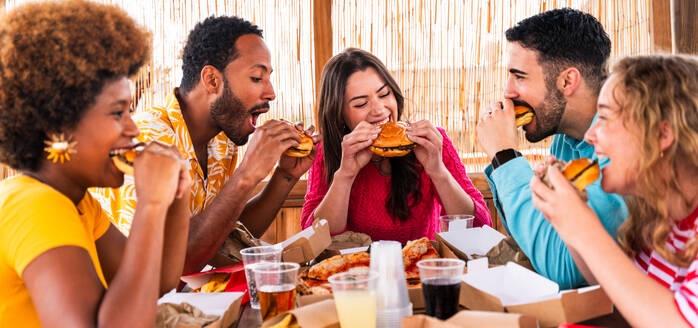 Multiethnic group of happy young friends having dinner barbecue party on rooftop at home - Multiracial cheerful young adult people having fun and bonding on a terrace balcony with city view, eating and drinking. - DMDF09192