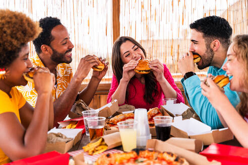 Multiethnic group of happy young friends having dinner barbecue party on rooftop at home - Multiracial cheerful young adult people having fun and bonding on a terrace balcony with city view, eating and drinking. - DMDF09193