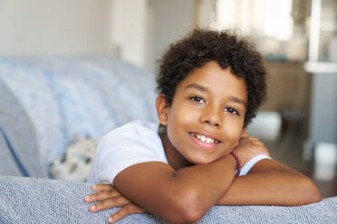 Closeup portrait of smiling African American teenager boy with black curly hair relaxing on sofa in living room at home - ADSF51192