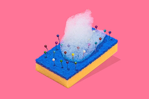 A creative representation of a blue and yellow scouring pad with colorful pins and bubbles of foam against a pink background - ADSF51193