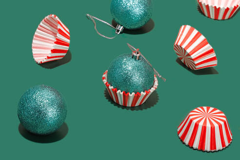Turquoise glitter Christmas baubles alongside red and white striped cupcake liners on a green surface - ADSF51196