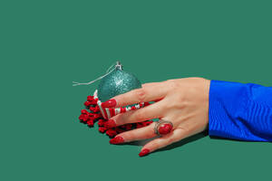 A hand adorned with a red ring holds a sparkly green Christmas ornament cupcake, against a green backdrop - ADSF51199