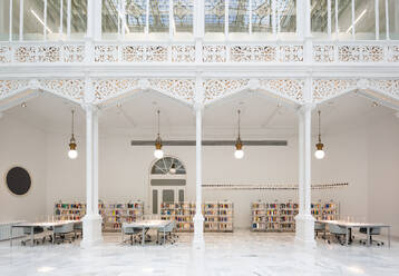 Illuminated lights hanging over empty tables and chairs with bookshelves in contemporary white library - ADSF51222