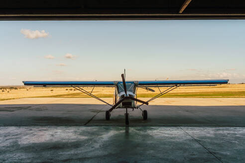 A single-engine aircraft is captured at rest in the hangar, with the open door framing a clear sky and the runway beyond - ADSF51223