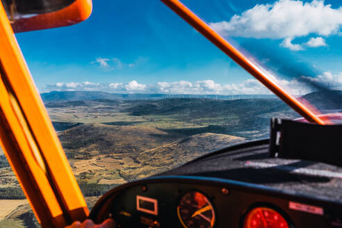 The interior view from the cockpit of an aircraft while a crop anonymous pilot is flying, with a vibrant blue and cloudy sky and expansive landscape stretching out below - ADSF51224