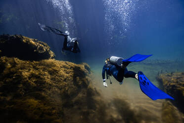 Two scuba divers swim through sunlit waters among the roots of mangroves in the unique ecosystem of Cancun, Mexico. - ADSF51227