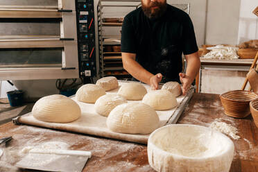 Crop anonymous red beard faceless make baker shaping raw dough with flour in tray while making loaf of bread at table in kitchen of bakery - ADSF51241