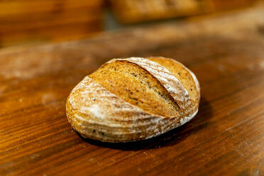 Closeup of freshly baked tasty loaf of bread with crispy crust placed on wooden table in kitchen at bakehouse - ADSF51245