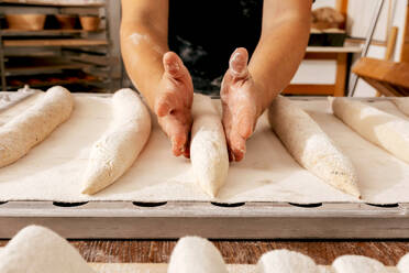 Crop anonymous faceless make baker shaping raw dough with flour in tray while making loaf of bread at table in kitchen of bakery - ADSF51248