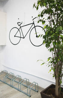 Black bicycle art on white wall over rack by fresh potted plant in creative modern office - ADSF51286