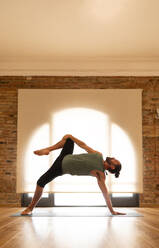 A male yogi demonstrates an intricate balance with a yoga pose, showing strength and flexibility in a tranquil studio setting. - ADSF51293