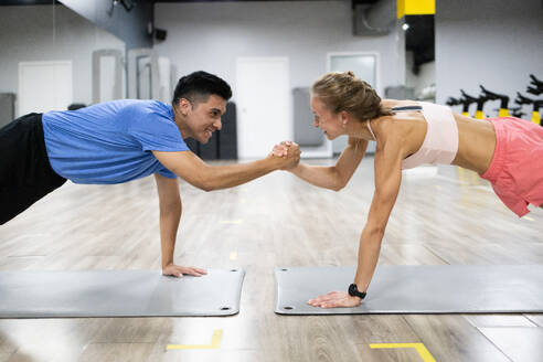 Two people engaged in a friendly fitness challenge, fist-bumping while doing planks in a modern gym. - ADSF51304