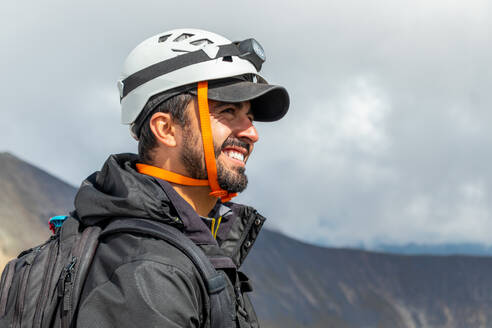 Close-up of a joyful male mountaineer wearing a safety helmet, set against the backdrop of the stunning Nevado de Toluca crater. - ADSF51311