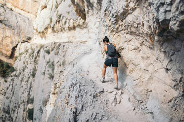 Back view full body of unrecognizable female hiker with backpack holding rope and trekking on majestic rocky mountain during weekend - ADSF51323