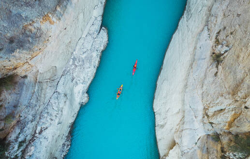 High angle view of unrecognizable people kayaking on blue narrow river flowing between rocky mountains during vacation at daytime - ADSF51324