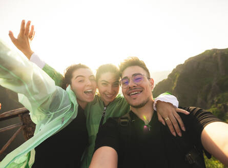 Portrait of cheerful Caucasian active young friends taking selfie looking at camera on mountain peak during sunrise at weekend hiking - ADSF51328