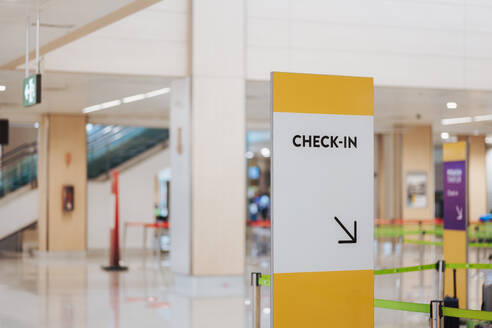 Yellow and white check-in directional sign at an airport with blurred background - ADSF51373