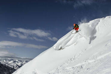 Full body of unrecognizable active person with skies jumping above snow covered mountain slope against blue sky during winter vacation on sunny day - ADSF51399