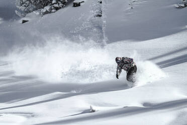 Full body of unrecognizable active hiker dressed in sportswear practicing snowboard mountain against cloudy sky during winter vacation on sunny day - ADSF51400