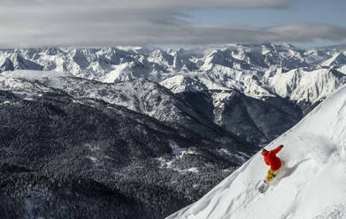 Back view of anonymous carefree person snowboarding on snowcapped mountain top against majestic view of mountains and sky during vacation - ADSF51401