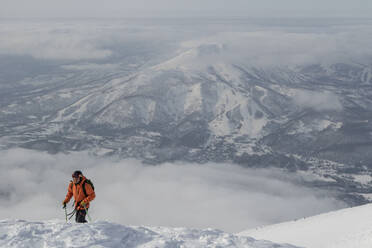 High angle from above view of male hiker walking with poles on beautiful snow covered mountain range against cloudy sky during winter vacation at Japan - ADSF51414