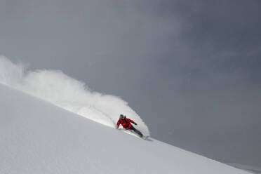 Full body of active unrecognizable person snowboarding on snow covered mountain slope with volcanic eruption in background during sunny day in winter vacation - ADSF51423