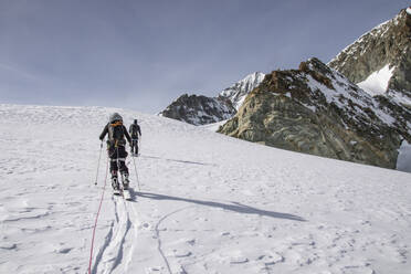 From below of anonymous men in warm clothes with ski following a guide rope on snow-covered landscape near majestic rocky mountain under blue sky in Zermatt, Switzerland - ADSF51445