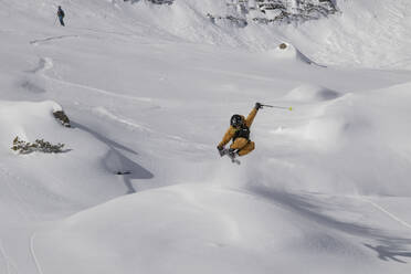 Full body of anonymous skier in warm suit jumping with skis on snow covered mountain slope during vacation at Swiss Alps - ADSF51456