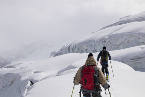 Back view of anonymous skiers in warm clothes skiing on snow-covered mountain on foggy day in Zermatt, Switzerland - ADSF51459