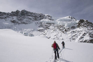 Back view of anonymous skiers in warm clothes skiing with guide rope on snow-covered mountain under blue sky in Zermatt, Switzerland - ADSF51461