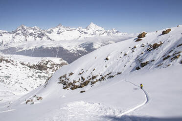 Aerial view of anonymous skiers in warm clothes skiing on snow-covered mountain slope against majestic rocky mountains under blue sky in Zermatt, Switzerland - ADSF51462