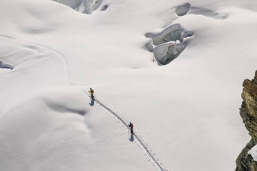 High angle of anonymous skiers in warm clothes making their way across the pristine, snow-blanketed surface of a glacier on sunny day in Zermatt, Switzerland - ADSF51463