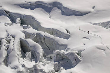 Aerial view of anonymous skiers in warm clothes making their way across the pristine, snow-blanketed surface of a glacier on sunny day in Zermatt, Switzerland - ADSF51464