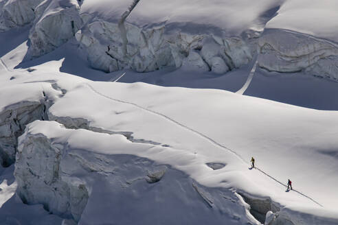 Aerial view of anonymous skiers in warm clothes making their way across the pristine, snow-blanketed surface of a glacier on sunny day in Zermatt, Switzerland - ADSF51466