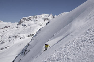 Anonymous Male Tourist looking down while snowboarding on majestic snow covered mountain slope against rocky mountains under blue sky in Zermatt, Switzerland - ADSF51468