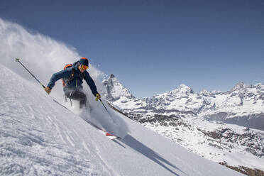 Side view of skier in warm suit skiing down on snow covered mountain slope against rocky mountains on sunny day during vacation at Swiss Alps - ADSF51469