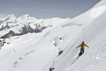 Full body of anonymous person with backpack descending while snowboarding on snow covered mountain slope against blue sky during vacation at Swiss Alps - ADSF51480