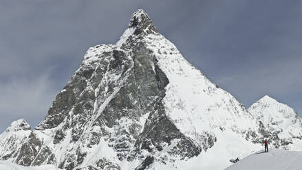 Back view of unrecognizable person with backpack skiing on snow covered land against majestic snowcapped mountain peak and sky at Swiss Alps - ADSF51483