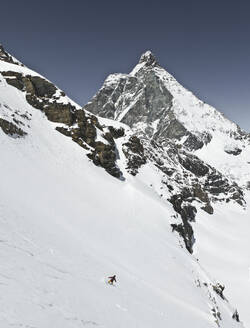 Full body of anonymous person descending while snowboarding on snow covered mountain slope against majestic mountain peak and blue sky during vacation at Swiss Alps - ADSF51485