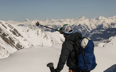 Side view portrait of anonymous active skier with poles and backpack on snow covered mountain slope under clear sky during sunny day in Canada - ADSF51488