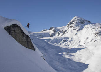 From below view of anonymous fearless snowboarder jumping above rock formation on snow covered landscape during winter holiday in Canada - ADSF51499