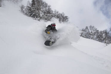 Unrecognizable adventure person snowboarding on snow covered hilly mountain against bare trees and sky while enjoying vacation in Japan - ADSF51504