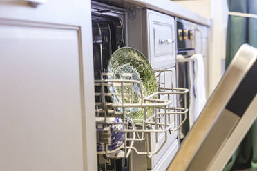 Close-up image of an open dishwasher loaded with sparkling clean dishware and kitchen utensils, showcasing domestic efficiency. - ADSF51513