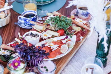 A lavish brunch table setup featuring fresh flowers, assorted cheese, smoked salmon, pastries, and beverages. - ADSF51514