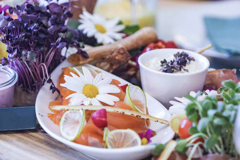 A colorful gourmet brunch spread featuring smoked salmon, edible flowers, fresh vegetables, dip, and citrus slices. - ADSF51516