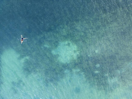 An aerial shot captures a single person floating peacefully in the translucent azure waters of the Mediterranean Sea along the Côte D'azur near Nice, France. - ADSF51519