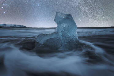 Majestic ice structure stands amidst the nocturnal waves of Diamond Beach, backdropped by a glittering starry sky in Iceland - ADSF51527