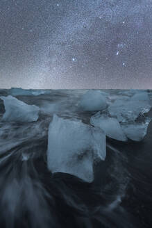 A serene night scene capturing ethereal icebergs against a backdrop of a star-studded sky at Diamond Beach, Iceland - ADSF51530