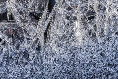 Close-up view of delicate frost crystals forming intricate patterns over a dark surface, evoking a cold winter's touch. - ADSF51537