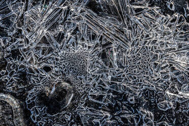 Close-up view of delicate ice crystals forming intricate patterns on a dark, frozen surface, showcasing the beauty of nature's winter artistry. - ADSF51538